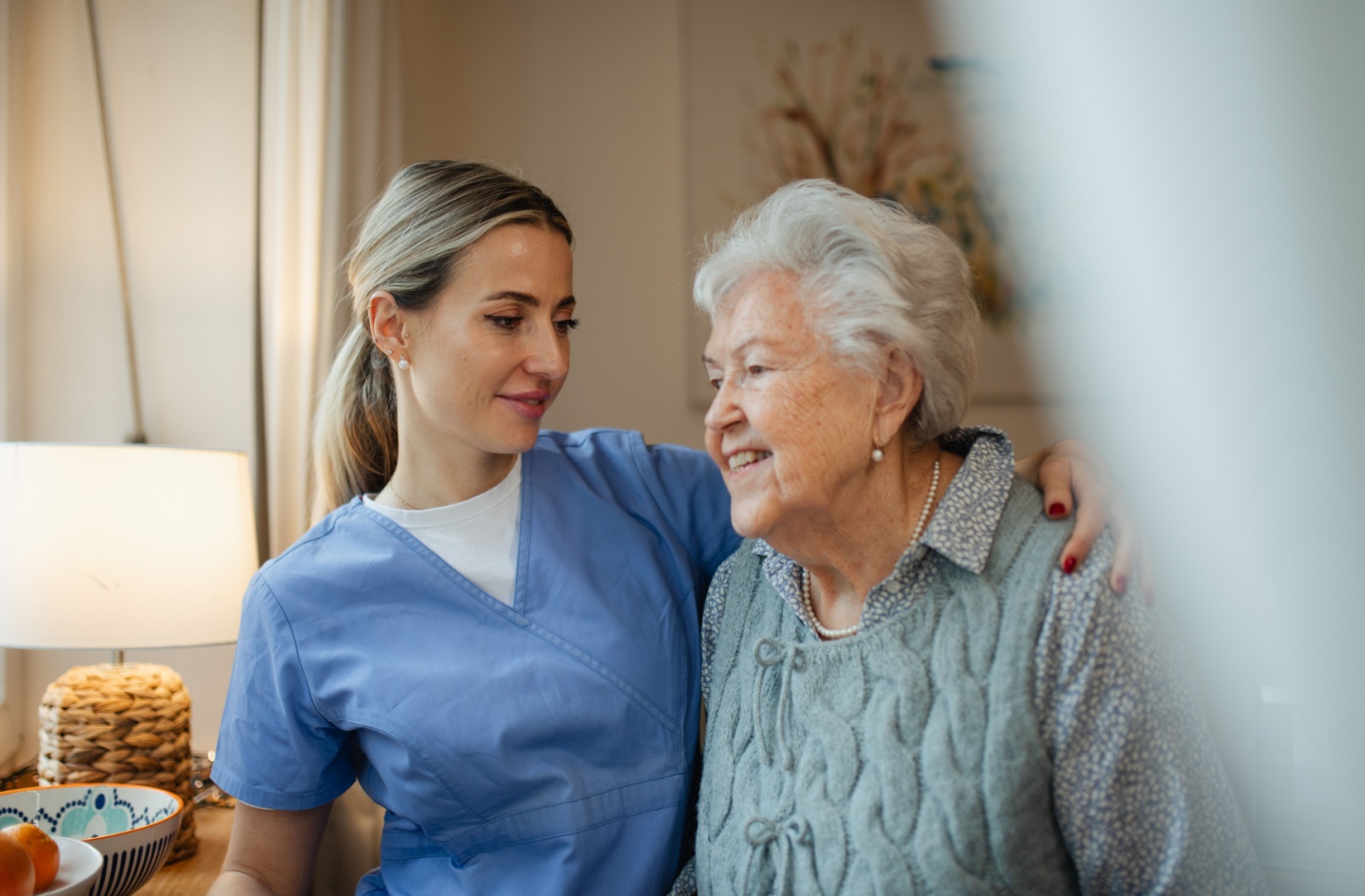 A nurse wraps their arm around a senior with dementia in memory care, smiling at them with genuine care and affection