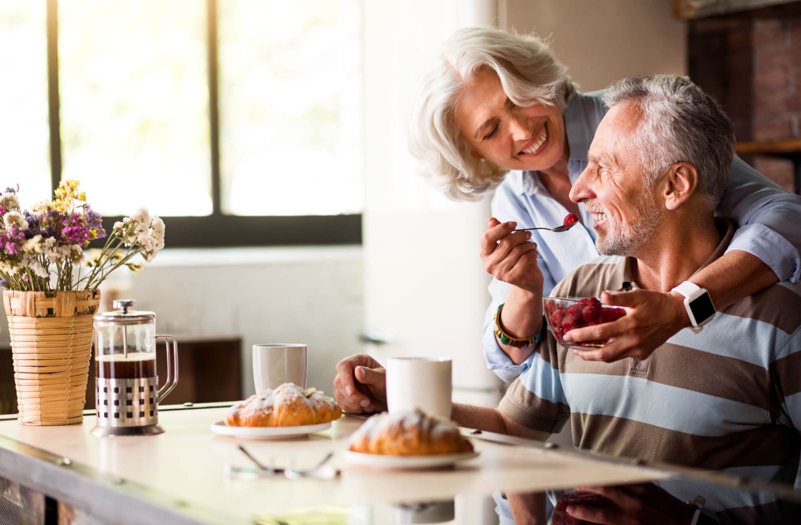 A senior couple embrace while eating raspberries during a morning snack to increase their daily fiber intake