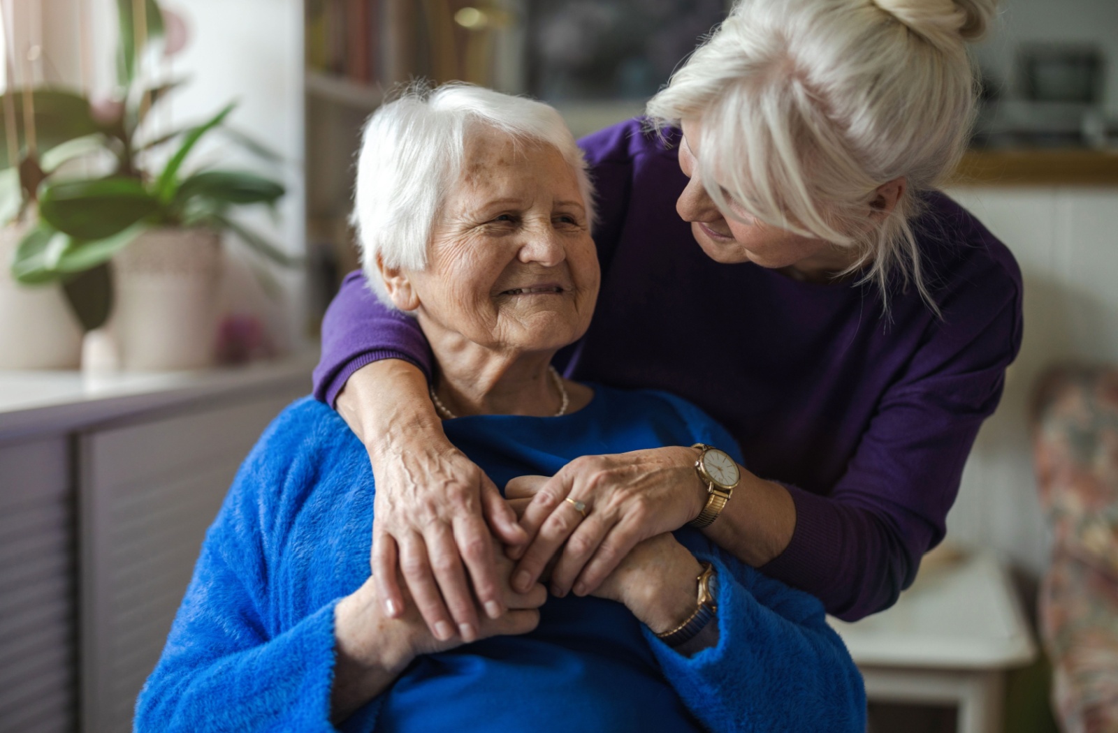 Adult daughter holding and smiling at her senior mom in memory care.
